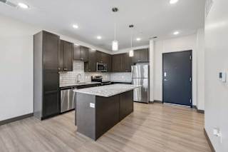 Modern apartment kitchen with dark cabinetry, granite island, stainless steel appliances, subway tile backsplash, and pendant lighting.