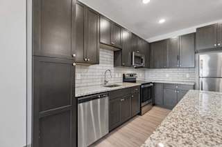 Apartment kitchen with dark cabinetry, granite countertops, subway tile backsplash, and stainless steel appliances.