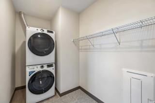 Apartment laundry and storage area with a stacked washer and dryer, carpeted floor, and wall-mounted wire shelving.