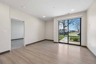 Open apartment living area with wood-style flooring, recessed lighting, and sliding glass doors leading to a ground-level patio.