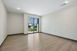 Empty apartment living area with wood-style flooring, recessed lighting, and sliding glass doors opening to a patio.