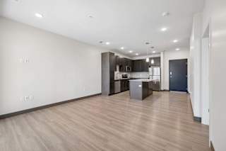 Open-concept apartment interior with wood-style flooring, recessed lighting, and a kitchen with an island and stainless steel appliances.