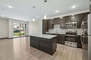Kitchen with granite island, dark cabinetry, stainless steel appliances, pendant lighting, and sliding patio doors.