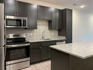 a kitchen with dark cabinets and light granite countertops and backsplash
