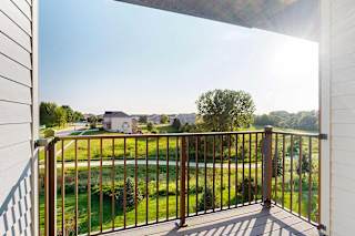 A balcony with a view of a green space, with houses in the distance.