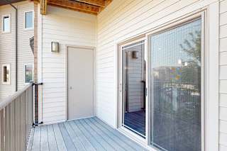 A balcony with a metal railing, a sliding glass door to the living room, and an outdoor storage closet.