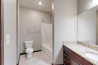 A long bathroom with a granite vanity sink, mirror, and tub shower.
