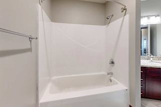 A white tub shower with a curved curtain rod, and a towel bar.