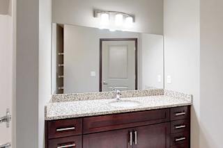 A bathroom with a granite vanity sink, an oversized mirror, and overhead lighting.
