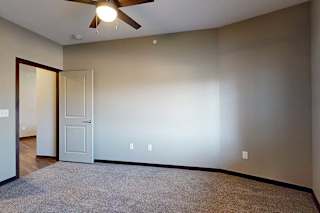 A carpeted bedroom with a ceiling fan and a door open to a hallway.