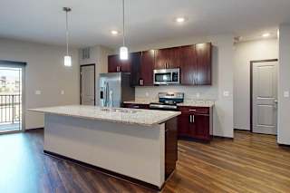 A modern kitchen with wooden cabinets, granite counters, a large central island, a pantry, and stainless steel appliances.