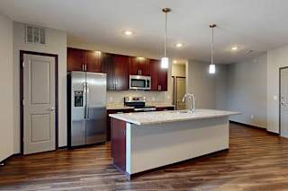 A modern kitchen with wooden cabinets, granite counters, a large central island, a pantry, and stainless steel appliances.