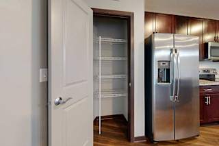 A kitchen pantry with built-in corner shelves next to a stainless steel fridge.
