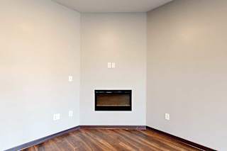 A living room with an electric fireplace and hardwood flooring.