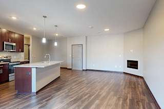 An open-concept living room with hardwood flooring and an electric fireplace, that connects to a modern kitchen with a large central island.
