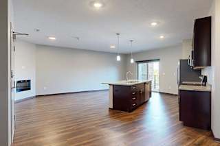 An open-concept living room with hardwood flooring and a sliding glass door to a balcony, that connects to a modern kitchen with a large central island.