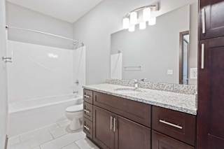 A bathroom with a granite vanity, dark wooden cabinets, and a tub shower.
