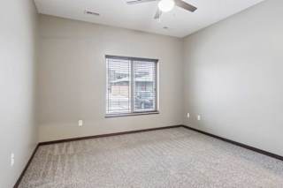 A carpeted bedroom with a ceiling fan and a window.