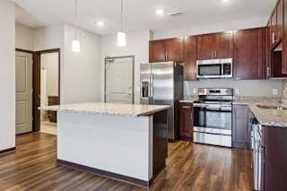 A kitchen with dark wood cabinets, granite countertops, a large island, and stainless steel appliances.