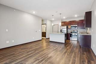 A living room with hardwood-style flooring and kitchen with dark wooden cabinets.