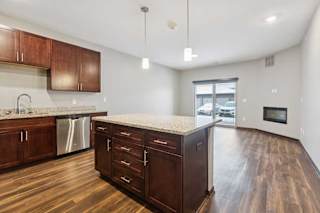 A kitchen with dark wooden cabinets and a large island, in front of a spacious living room.