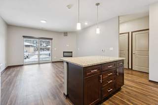 A kitchen with dark wooden cabinets and a large island, in front of a spacious living room.