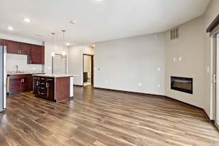 A living room with hardwood-style flooring and kitchen with dark wooden cabinets.