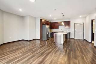 A living room with hardwood-style flooring and kitchen with dark wooden cabinets.