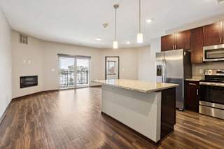 A kitchen with dark wooden cabinets and a large island, in front of a spacious living room.