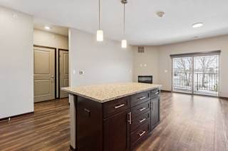 A kitchen with dark wooden cabinets and a large island, in front of a spacious living room.