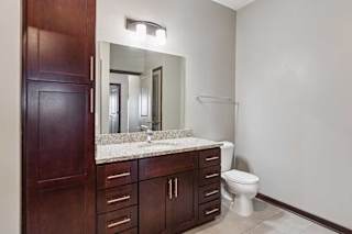 A bathroom with a granite vanity, dark wooden cabinets, and a large mirror with overhead lighting.