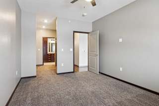 A carpeted bedroom with a ceiling fan and an open walk-through closet to a connected bathroom.