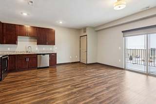 A living room with hardwood-style flooring and kitchen with dark wooden cabinets.