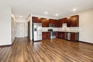 A living room with hardwood-style flooring and kitchen with dark wooden cabinets.