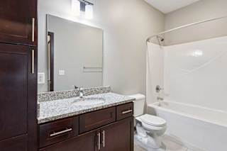 A bathroom with a granite vanity, dark wooden cabinets, and a tub shower.