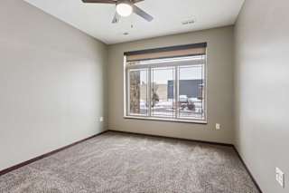 A carpeted bedroom with a ceiling fan and a floor-to-ceiling window.