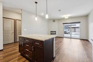 A kitchen with dark wooden cabinets and a large island, in front of a spacious living room.