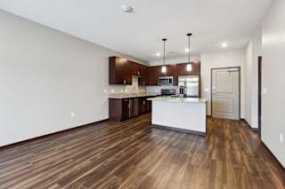 A living room with hardwood-style flooring and kitchen with dark wooden cabinets.