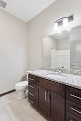 A bathroom with a granite vanity, dark wooden cabinets, and a walk-in shower.