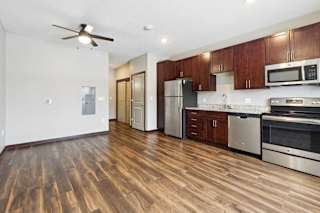 A living area with a ceiling fan, open to a kitchen with dark wooden cabinets.