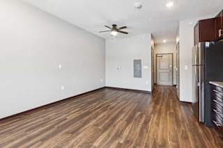 A living area with a ceiling fan, open to a kitchen with dark wooden cabinets.