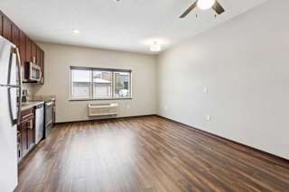 A living area with a ceiling fan, open to a kitchen with dark wooden cabinets.