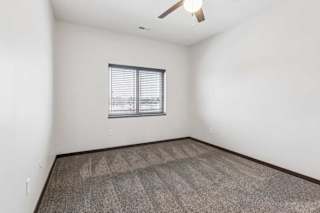 A carpeted bedroom with a ceiling fan and a window.