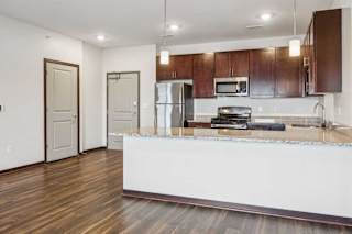 A kitchen with dark wood cabinets, granite countertops, and stainless steel appliances next to the front door and entryway closet.