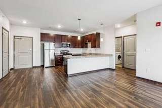 A living room with hardwood-style flooring and kitchen with dark wooden cabinets.