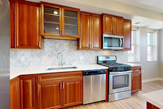 A kitchen with cherry-stained wooden cabinets, light quartz countertops, and stainless steel appliances.