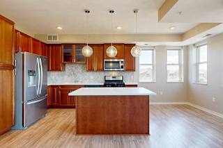A kitchen with cherry-stained wooden cabinets, light quartz countertops, stainless steel appliances, and an island with pendant lighting.