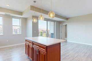 A kitchen island with cherry-stained wooden cabinets and a light quartz countertop, in front of a spacious living room.