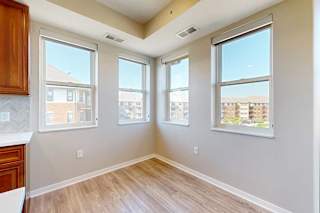 A dining room with hardwood-style flooring, and several large windows for natural light.