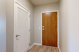 An entryway with a wooden front door and a white slatted door to a laundry room.
